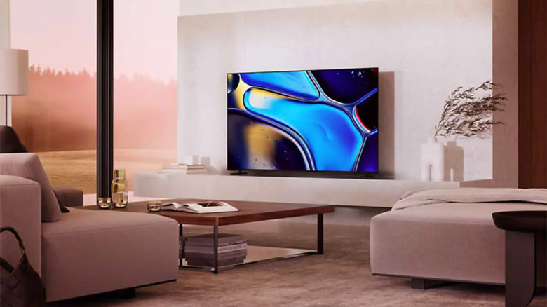 A Sony Bravia 8 OLED TV positioned on a media console in a warm, lit living room.