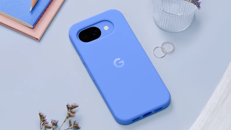 A blue Google Pixel 10a smartphone lying flat on a minimalist table surface.