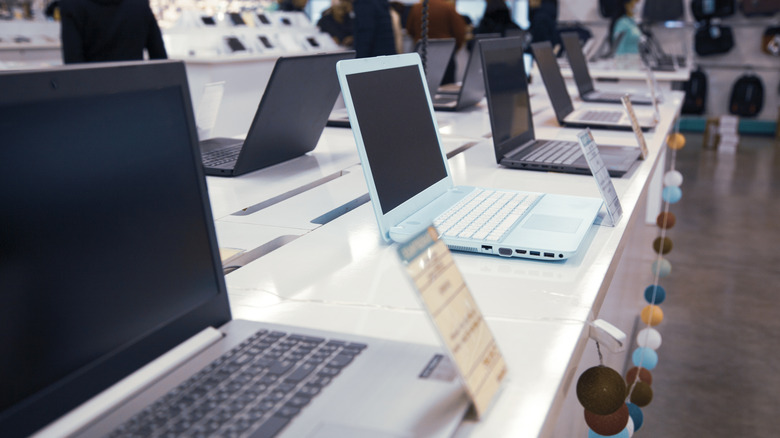 Multiple laptops displayed on shelves in an electronics retail store.