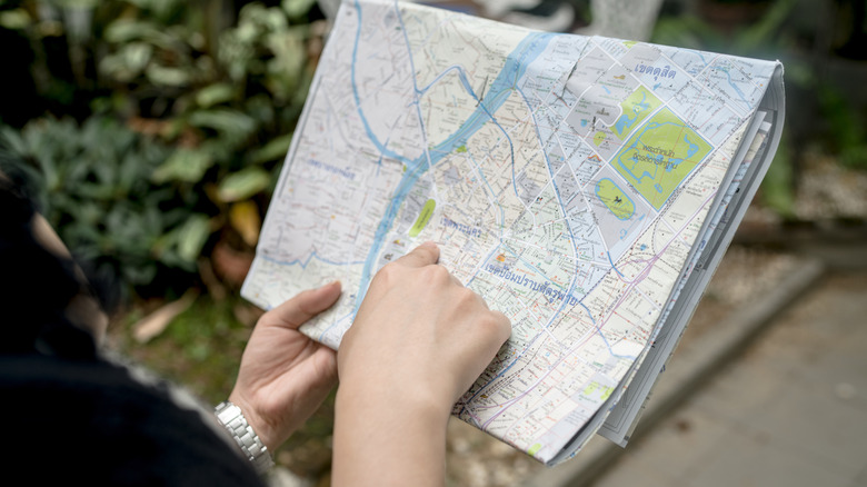 A woman standing on a city street holding a large unfolded paper map.