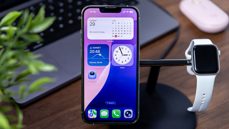 A close-up of an iPhone on a charging stand alongside an Apple Watch, displaying widgets.