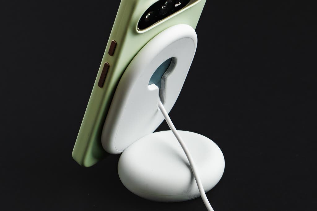 A modern smartphone magnetically attached to a wireless charging stand.