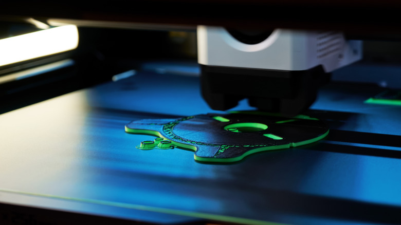Macro shot of a 3D printer nozzle extruding green filament to create a 3D part.