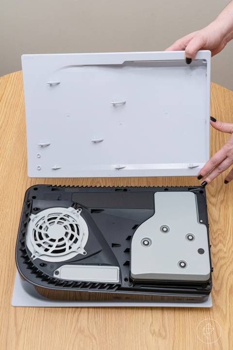 A person demonstrating the manual removal of the PlayStation 5 side panel while the console is in a horizontal position.
