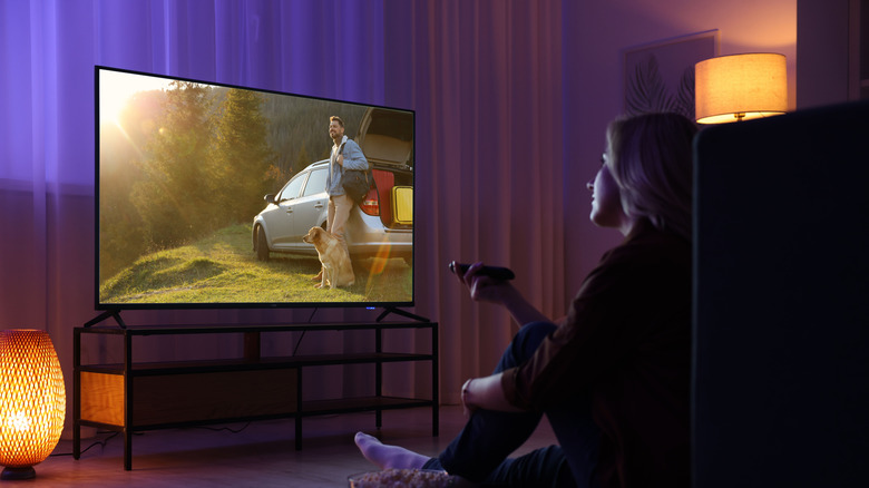 A woman watching a high-contrast movie on a large screen in a dimly lit living room.