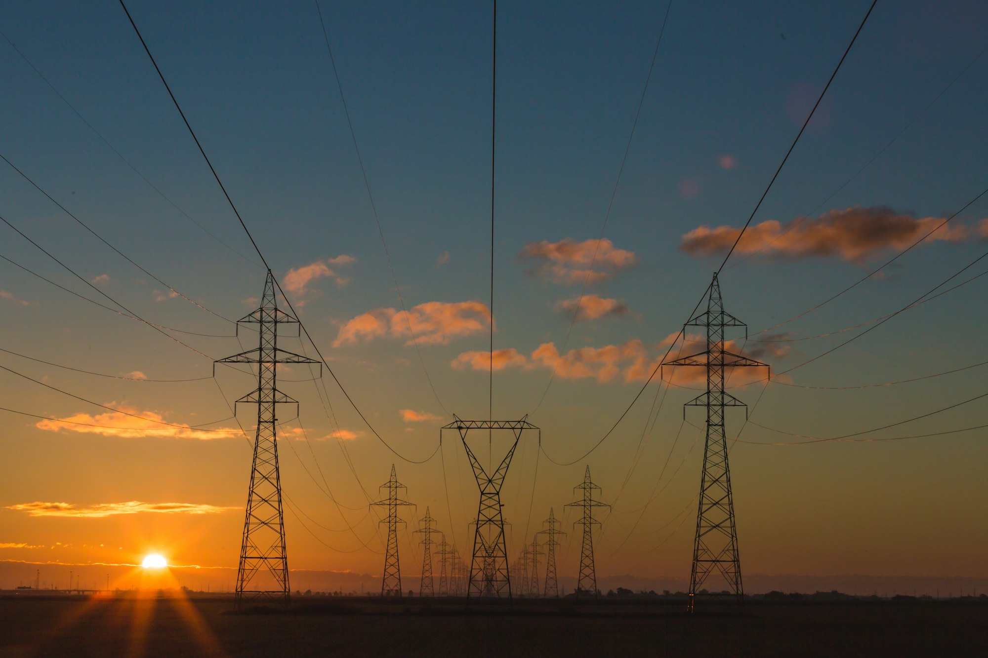 High-voltage power transmission lines stretching across a field under a clear sky.
