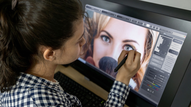 A creative professional using a tablet and stylus to edit photos in a software environment.