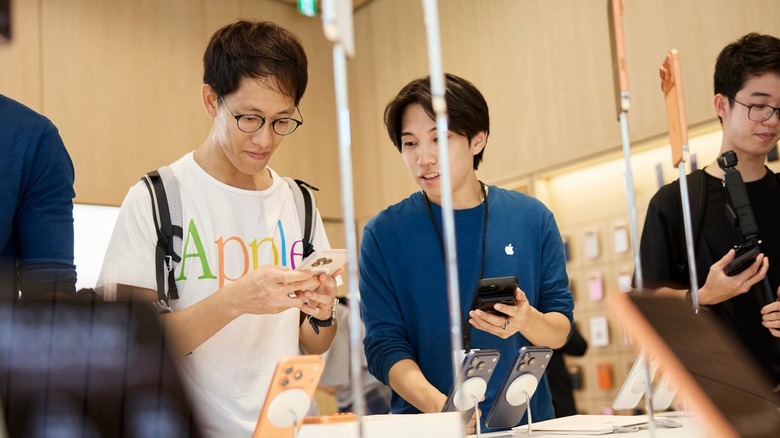 An Apple Store specialist in a blue shirt pointing at an iPhone screen while interacting with a customer.