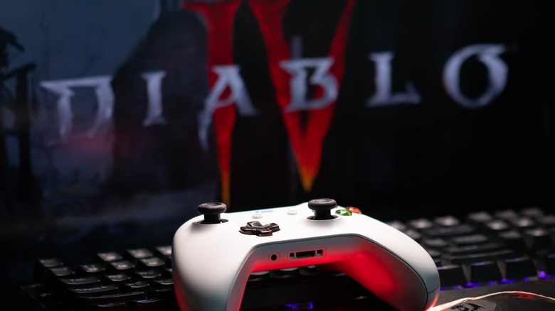 An Xbox controller placed on a mechanical keyboard in front of a PC monitor showing a video game.
