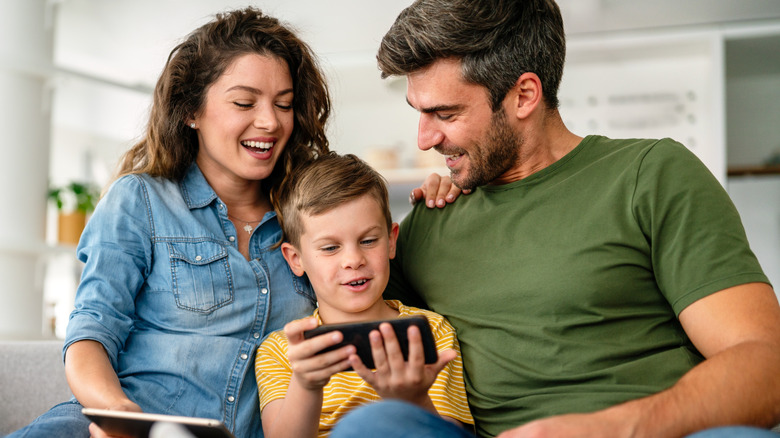 A family of four sitting on a couch together, all engaged with their smartphones and tablets.