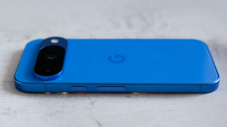 A blue Google Pixel 10 smartphone resting on a marble-textured surface.