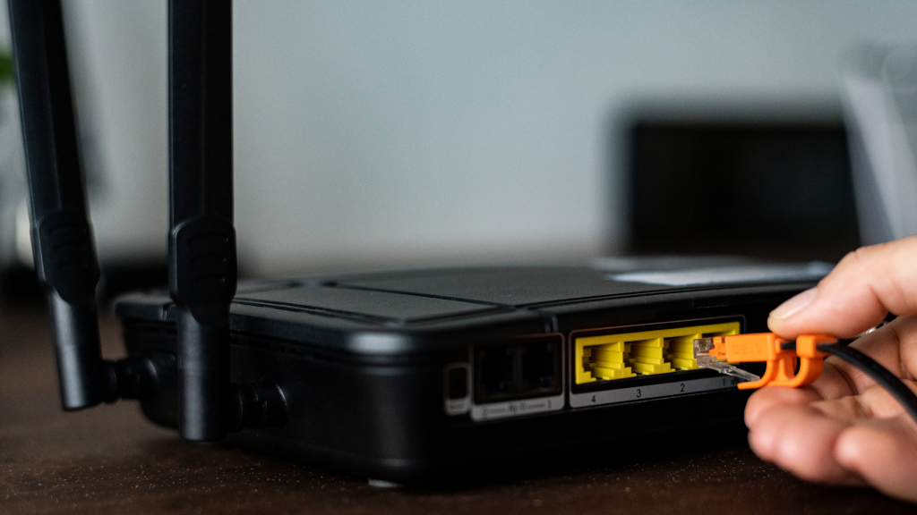 A person's hand pressing the power button on a home internet router.