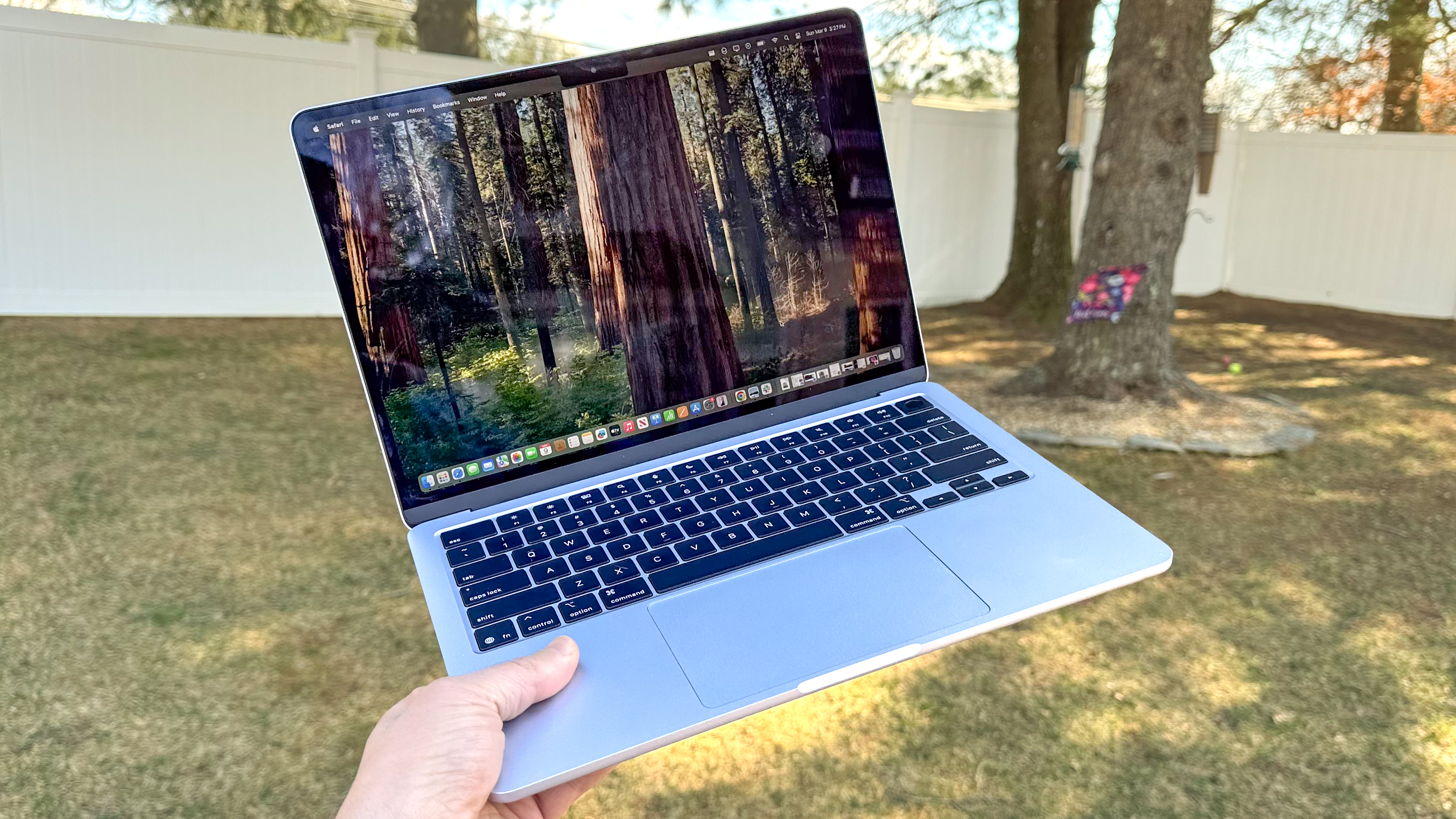 A person holding a silver MacBook Air 13-inch outdoors.