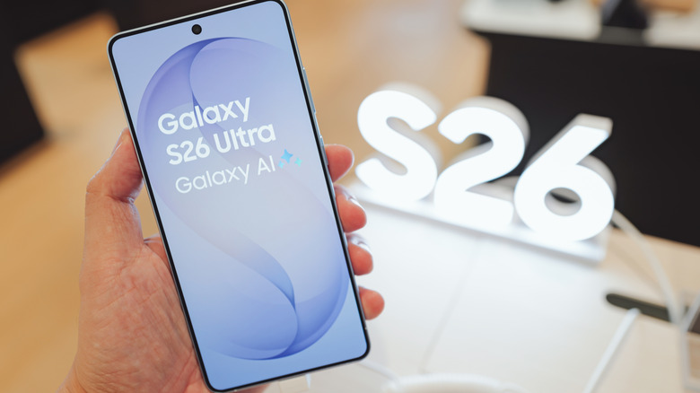 A hand holding the Samsung Galaxy S26 Ultra flagship phone with a glowing S26 light effect in the background.