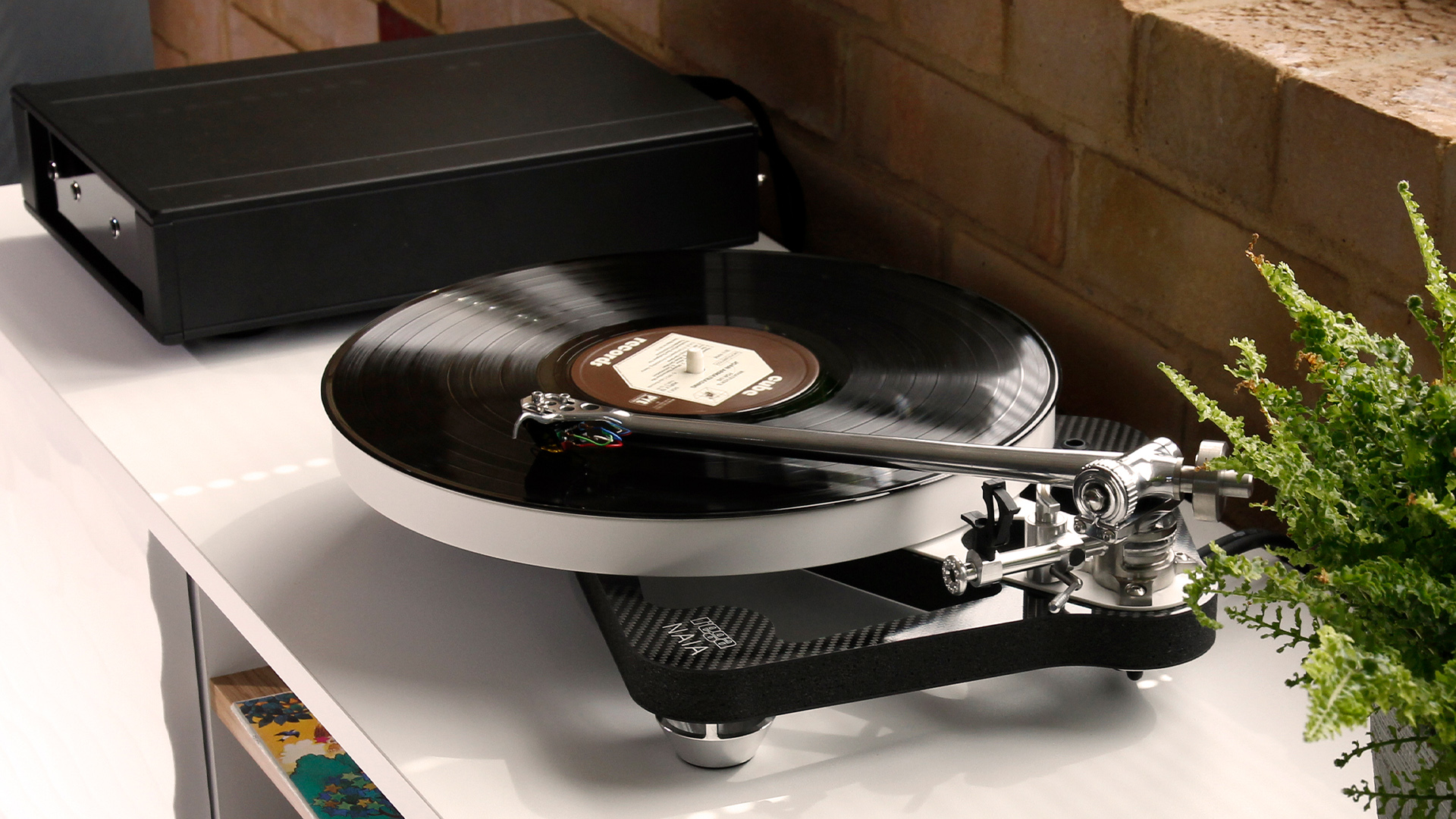 A Rega Naia skeletal design turntable sitting in a modern, well-lit living room.