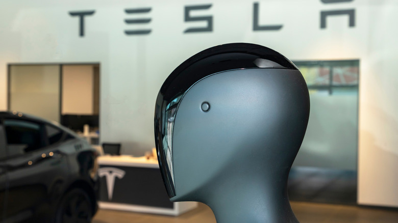 Side profile of the Tesla Optimus humanoid robot head and torso against a Tesla logo.