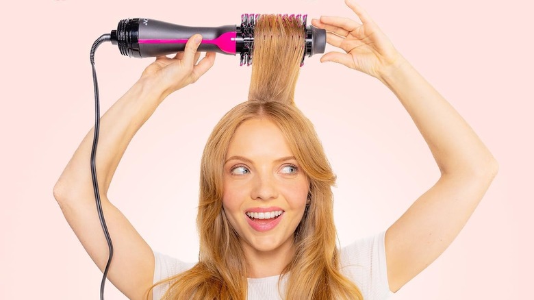 A woman with high-volume blonde hair using the Revlon One-Step Volumizer brush.