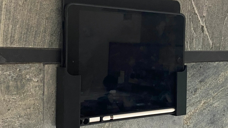 A tablet mounted securely to a wall using a white custom 3D printed bracket.