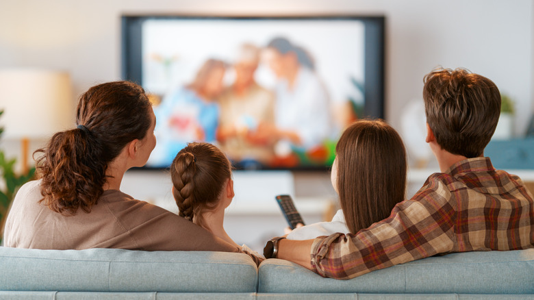A family relaxing on a sofa in front of a TV displaying high-resolution personal photos.