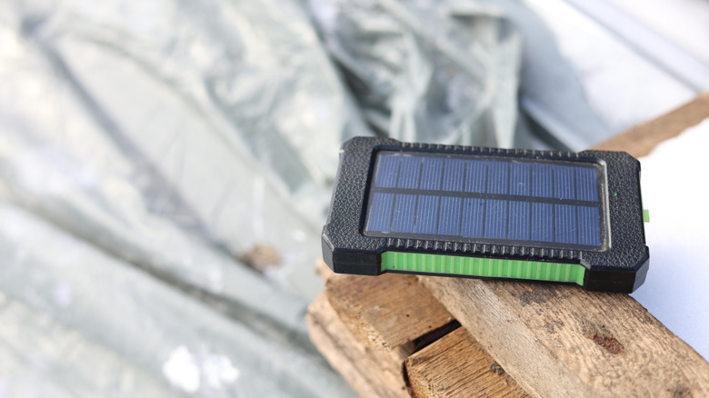 A single-panel portable solar power bank resting on a wooden surface under bright direct sunlight.