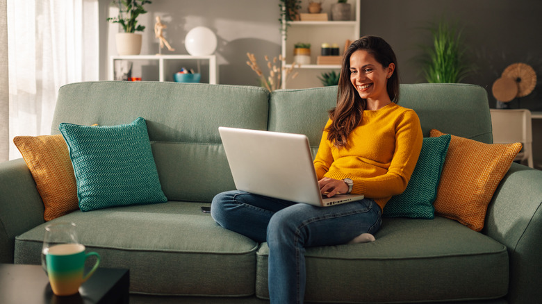 A woman using a laptop and smartphone simultaneously while sitting comfortably at home.