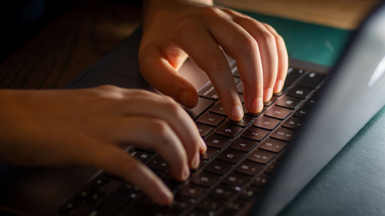 Close-up of a person's hands typing quickly on a modern laptop keyboard.