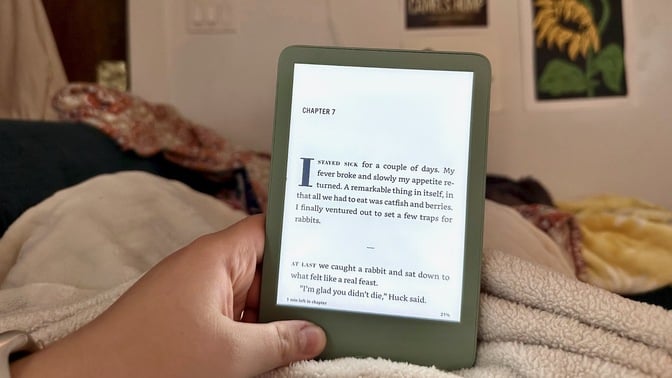 A person holding a standard entry-level Amazon Kindle in their lap while reading.