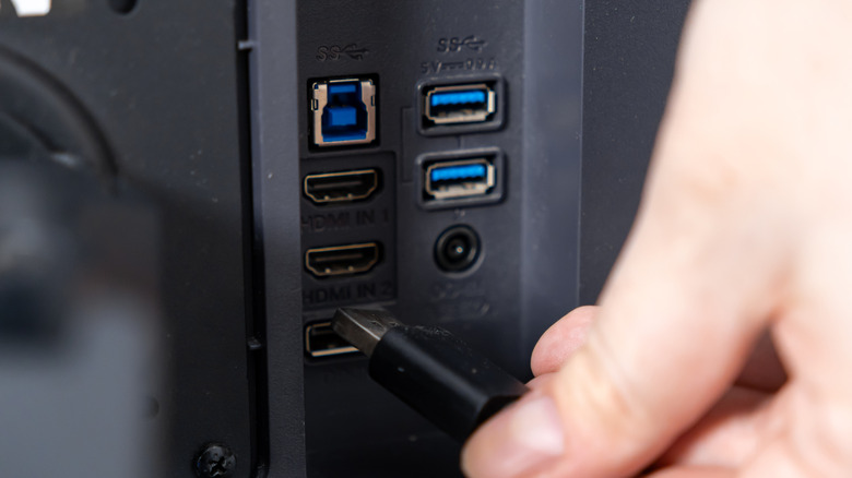 A hand plugging a high-speed HDMI cable into the back of a television panel.