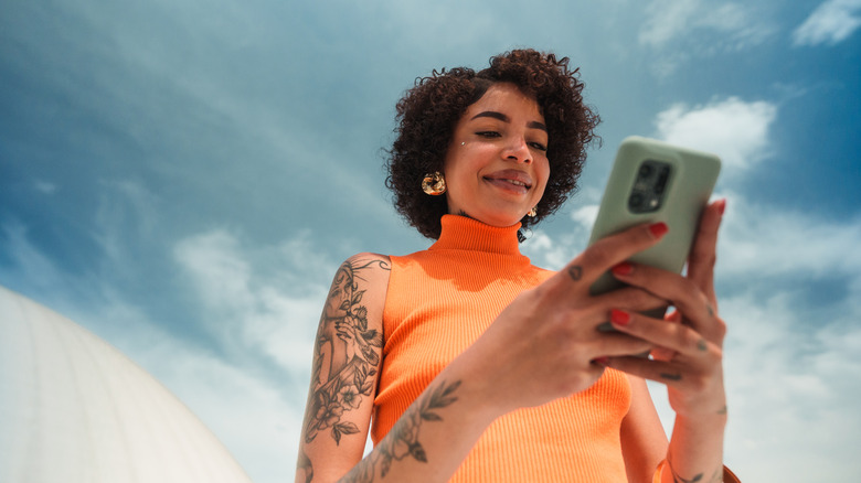 A person holding a smartphone outdoors with bright sun illuminating the display.