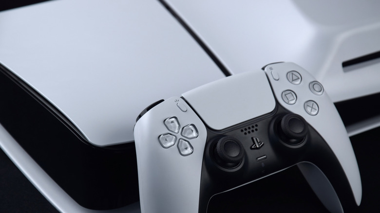 Close-up of a white PlayStation 5 console and a DualSense controller on a neutral surface.