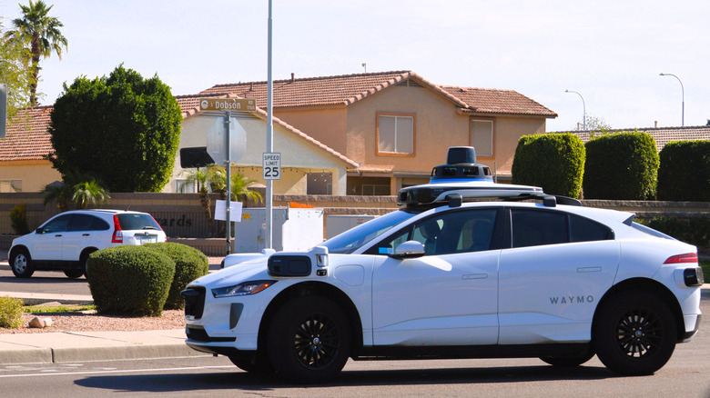 A white Waymo self-driving vehicle navigating a residential street in Phoenix, Arizona.