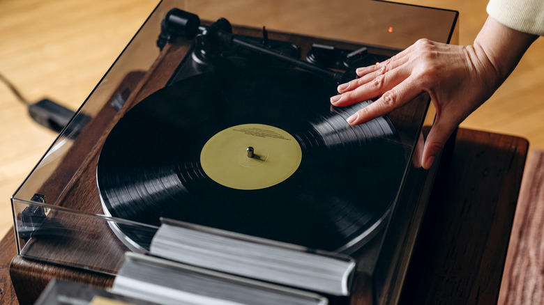 A person's hands closing the dust cover of a turntable to begin playing a record.